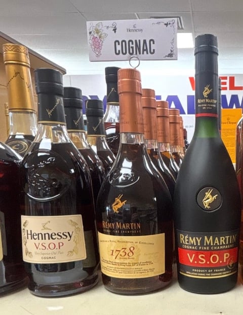 Display of premium cognac bottles including Hennessy and Remy Martin brands with wooden corks and a cognac sign above