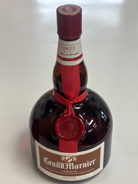 Bottle of Grand Marnier liqueur with burgundy top, red ribbon seal, and white label on dark glass bottle