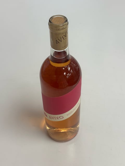 A bottle of AVVO wine with a cork stopper, featuring a pink label and reddish liquid inside, photographed against a white background.