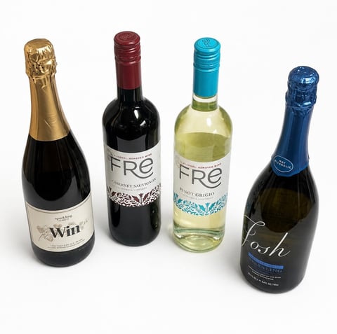 Four wine bottles in a row: gold-capped champagne, red FRE wine, white FRE wine, and blue-capped sparkling wine