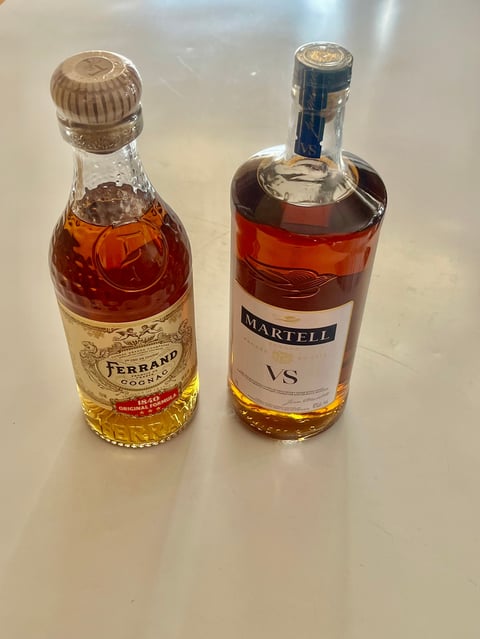 Two cognac bottles side by side: Ferrand on the left with a small bottle and wired cap, and Martell VS on the right with a larger bottle and black cap