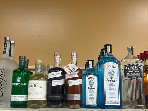 Collection of assorted liquor bottles including gin, whiskey, and other spirits arranged on a shelf against a beige wall