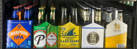 Assorted beer bottles displayed in a row including Harpoon IPA, Land Shark, and other craft beers on a dark shelf