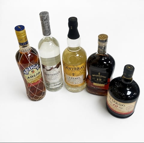 Five bottles of alcohol including rum, vodka, and brandy arranged in a line against a white background
