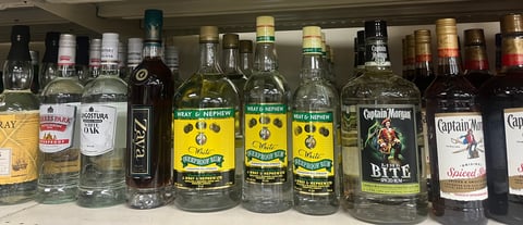 Assorted bottles of spirits and liqueurs displayed on a shelf, including rum, vodka, and other alcoholic beverages in various glass bottles