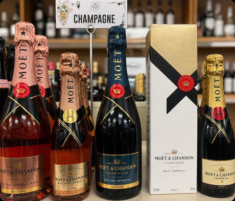 Collection of Moet and Chandon champagne bottles in various styles displayed with gift packaging and signage against a blurred bar background