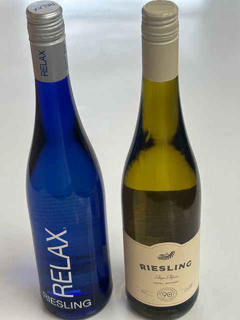 Two Riesling wine bottles side by side: a blue Relax Riesling on the left and a traditional Riesling with pale yellow-green wine on the right