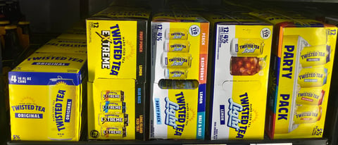 Variety of Twisted Tea beverage cases and multi-packs displayed on store shelf, showing yellow and white packaging with different flavors.