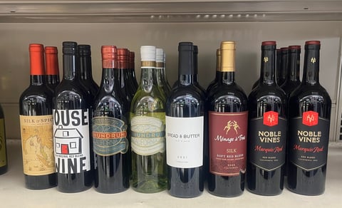 Collection of wine bottles displayed on a shelf, featuring various red wines with different labels and bottle designs