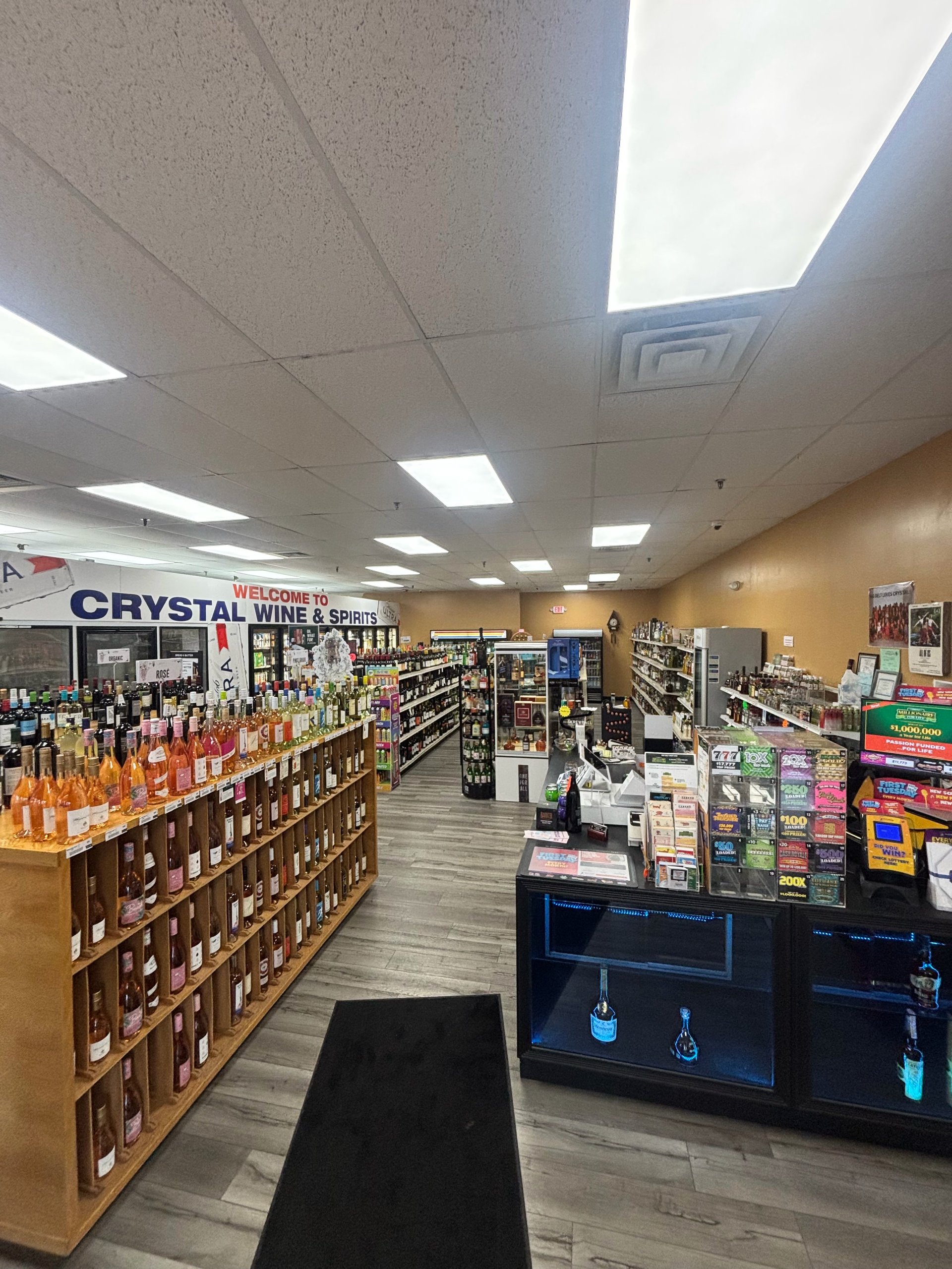 Interior of a liquor store with shelves of wine bottles on the left, checkout counter on the right, and product displays throughout