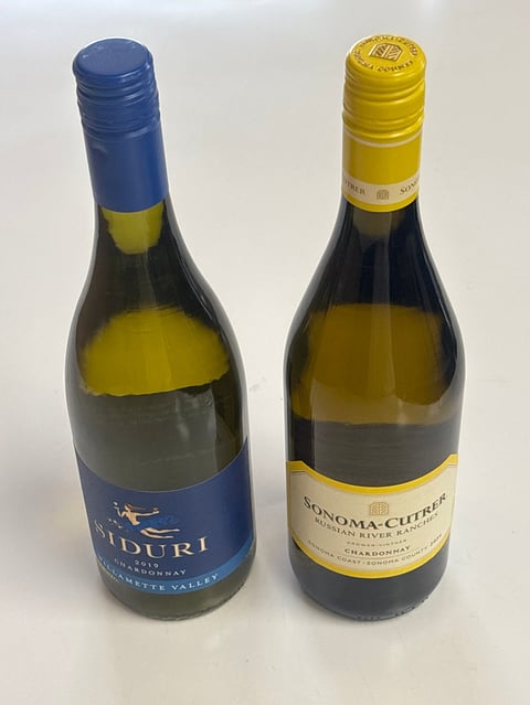 Two wine bottles side by side: left bottle with blue capsule and label, right bottle with yellow capsule and cream-colored label.